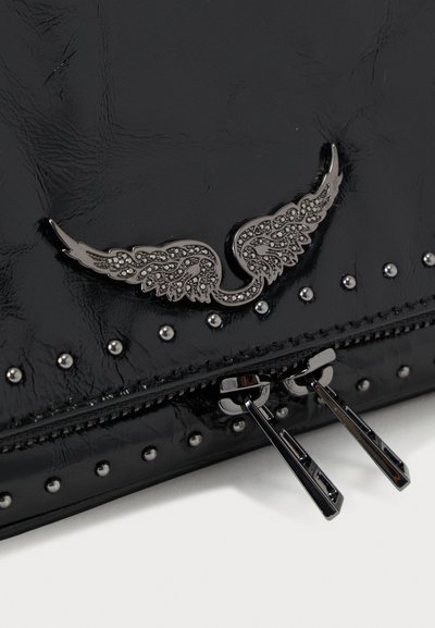 Μαύρη τσάντα χειρός από γυαλιστερό δέρμα με ασημί λεπτομέρεια σε σχήμα φτερού, διακοσμημένες με τρουκς και διπλά φερμουάρ στην κορυφή.