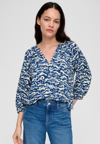 Blauw-wit geblokte blouse met een V-hals, lange uitpuf mouwen en een relaxte pasvorm, gecombineerd met donkerblauwe jeans.