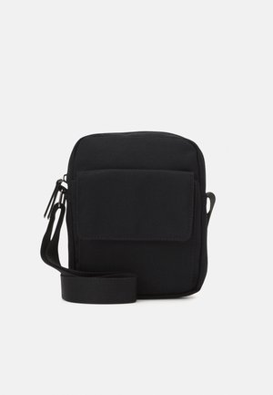 Sac bandoulière carré noir avec poche avant à rabat et bandoulière réglable sur un fond clair uni.