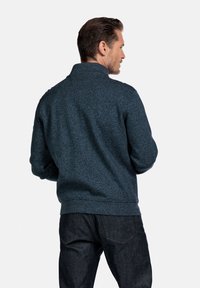 Dunkelblauer Strickpullover mit hohem Kragen, gerippten Manschetten und Saum, strukturiertem Stoff und lockerer Passform, kombiniert mit dunklen Jeans.