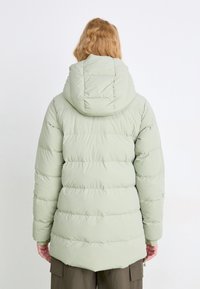 Giacca puffer verde chiaro con cappuccio, caratterizzata da cuciture orizzontali e polsini a coste. Texture liscia e tasca con zip in vita.