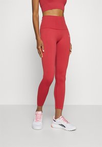 Leggings rossi a coste con alta vita, abbinati a sneakers bianche con dettagli rosa. Il design enfatizza una silhouette aderente.