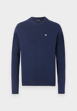 Tengerészkék hosszú ujjú, kerek nyakú pulóver bordázott mandzsettákkal és kis fehér sas logóval a bal mellkasnál.