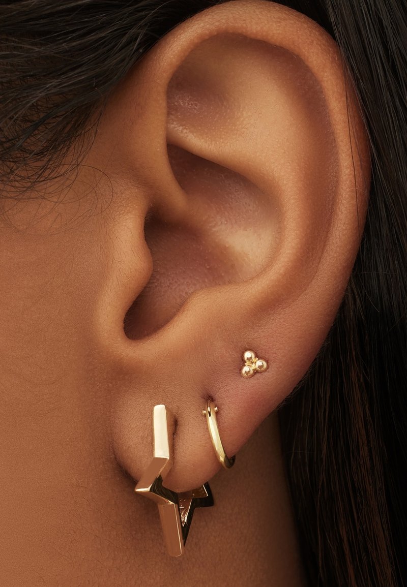 Boucles d'oreilles en ton doré sur une oreille : l'une présente un design géométrique en forme d'éclair ; l'autre est une petite créole avec trois accents de perles.