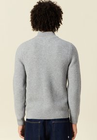 Suéter de punto gris con un cuello redondo acanalado y un patrón texturizado. Terminado con puños y dobladillo acanalados, mostrando un diseño casual.