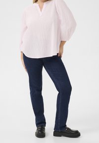 Jasnoróżowa, fakturowana bluzka z dekoltem w serek i rękawami o długości trzy czwarte, zestawiona z ciemnoniebieskimi dżinsami i czarnymi mokasynami na platformie.