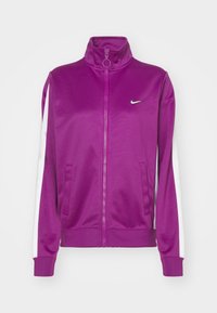 Lila dragkedjejacka med hög krage, vit sidrand, tillverkad av ett slätt material och med en liten Nike-logotyp på bröstet.