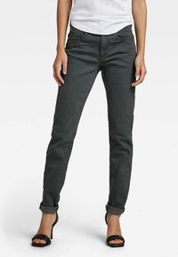 Jeans de mezclilla gris oscuro con un corte ajustado, puños enrollados y diseño de cinco bolsillos. Llevados con una camisa blanca y sandalias de tacón negro.