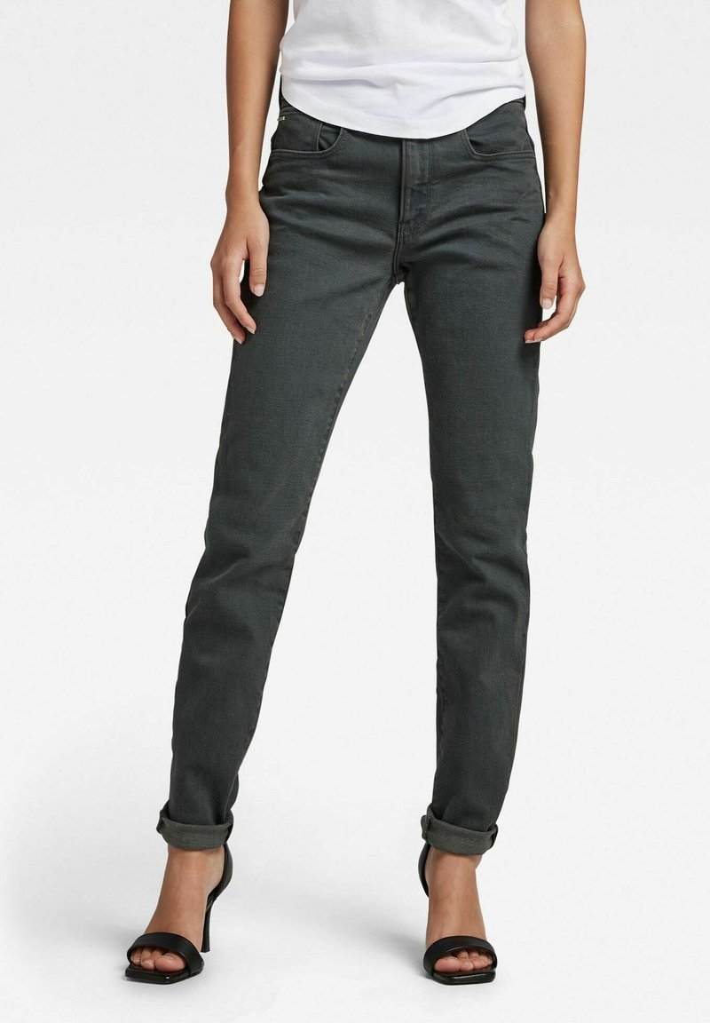 Jeans de mezclilla gris oscuro con un corte ajustado, puños enrollados y diseño de cinco bolsillos. Llevados con una camisa blanca y sandalias de tacón negro.
