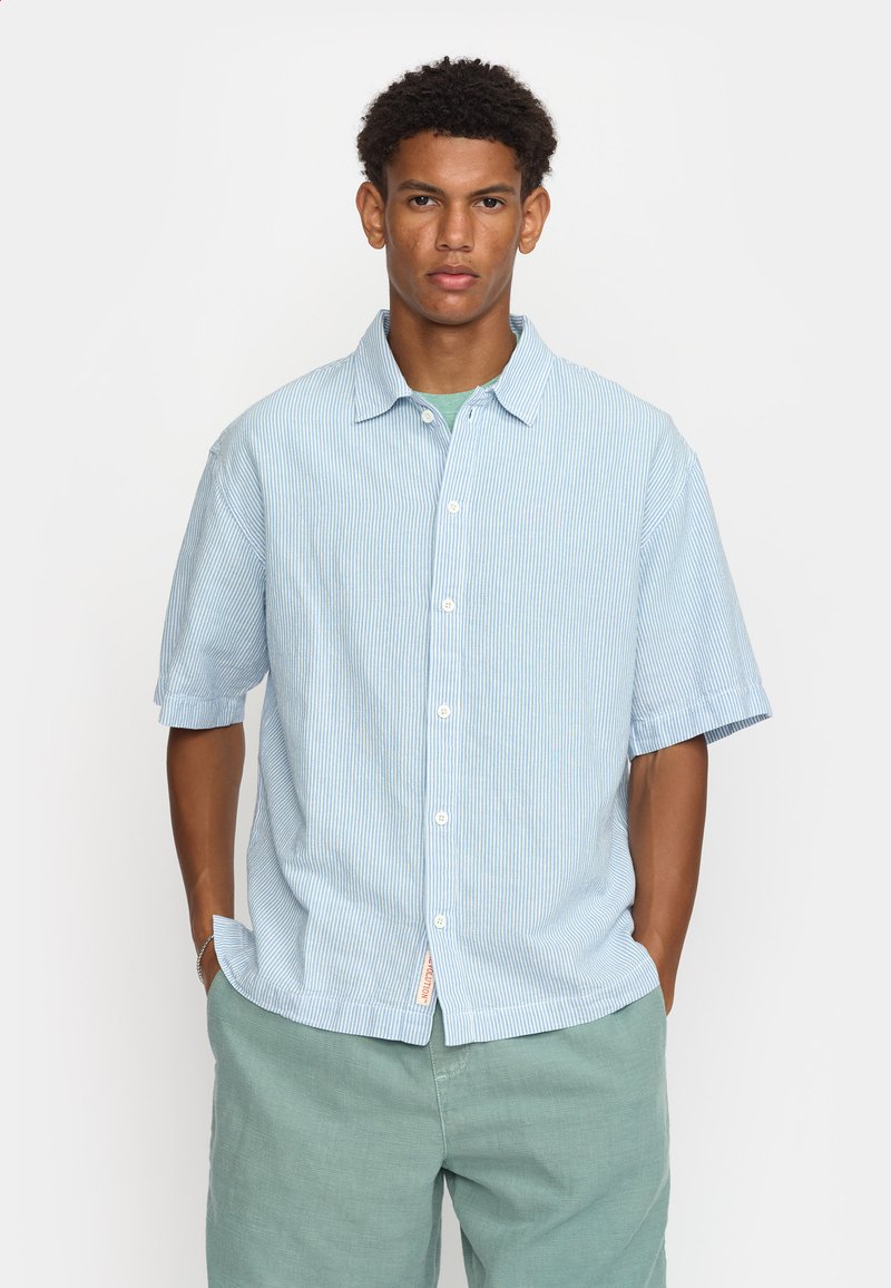 Camisetta a maniche corte di colore azzurro chiaro con righe bianche verticali; presenta un colletto con bottoni e un orlo dritto. Realizzata in tessuto leggero.