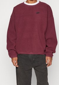 Sudadera de forro polar burdeos con superficie texturizada, cuello redondo y logo de Nike negro en el pecho. Puños y dobladillo acanalados.