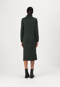 Abito di maglina verde scuro con colletto alto, maniche di lunghezza media e vestibilità affusolata, realizzato in un materiale morbido e testurizzato.