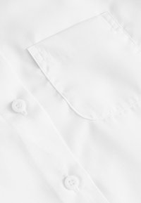 Hvid skjorte stof med en lomme og en knapdetalje. Texturen er glat, og materialet synes let med en ren finish.