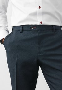 Pantaloni navy din material texturat, cu închidere prin buton și buzunare. Asortați cu o cămașă albă cu butoane roșii la accent.