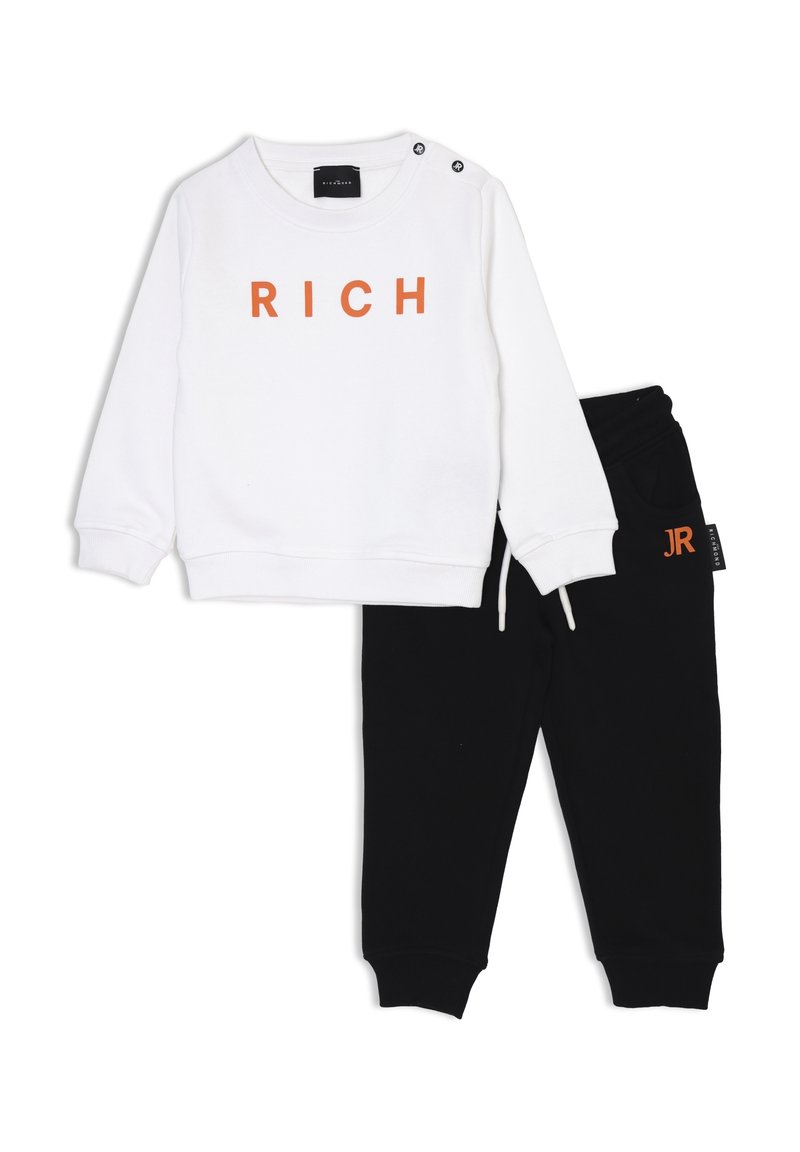 Felpa bianca con la scritta "RICH" in lettere arancioni e pantaloni della tuta neri con vita regolabile e dettaglio del logo. Materiale morbido, design casual.