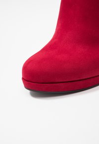 Rode suède enkellaars met een afgeronde neus en een gladde textuur, voorzien van een verhoogde naad en een zwarte rubberen zool.