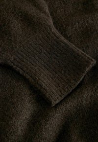 Detalle de una prenda de lana marrón oscuro que presenta un puño acanalado y una tela suave y texturizada. La superficie muestra ligeras variaciones en color y textura.