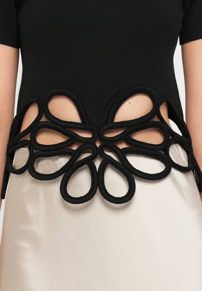 Black top featuring a textured floral design made of overlapping loops at the waist, paired with a smooth, light-colored lower garment.