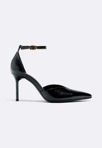 Sort spids tå pumps med ankelrem og guldspænde, blank finish, stiletthæl, sidevisning på hvid baggrund.