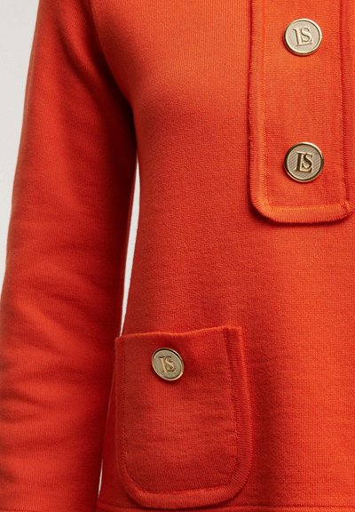 Roter Strickpullover mit Rundhalsausschnitt, ausgestattet mit goldenen Knöpfen, einer Brusttasche und lockerem Schnitt. Strukturierter Stoff mit glatter Oberfläche.