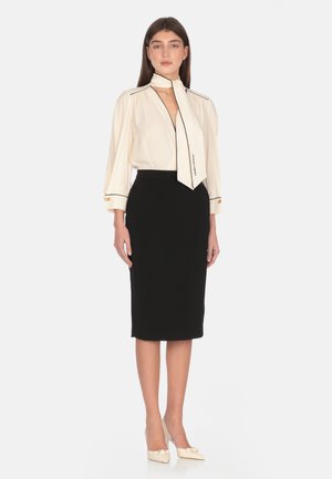 Blusa avorio con bordi neri, maniche lunghe e una sciarpa annodata; abbinata a una gonna a tubino nera aderente. Tacchi crema con dettaglio a fiocco.
