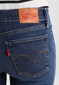 Primer plano de unos vaqueros con una etiqueta de Levi Strauss destacada en la cinturilla, presenta una pestaña roja en el bolsillo trasero.
