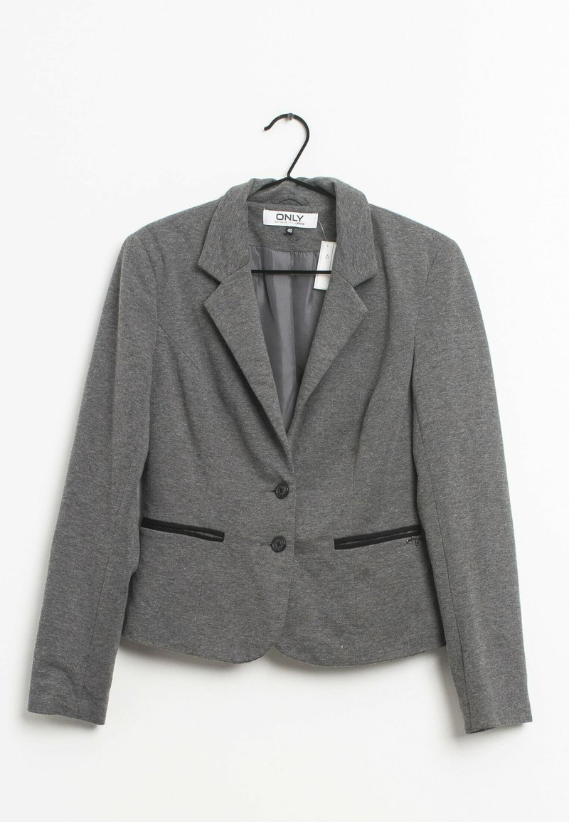 Blazer gris pour femme avec deux boutons, revers crantés et poches avant zippées suspendu sur un cintre noir.