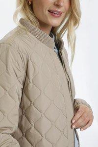 Veste bomber beige matelassée avec col côtelé et fermeture éclair visible, présentant une texture lisse et un motif en diamant prononcé.