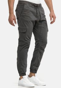 Gray cargo pants with elastic cuffs, drawstring waist, multiple pockets, and a smooth texture. Paired with white sneakers.