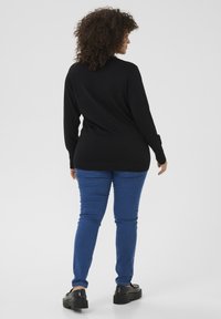 Black long-sleeve top with a relaxed fit, paired with blue skinny jeans and black platform shoes, viewed from the back.