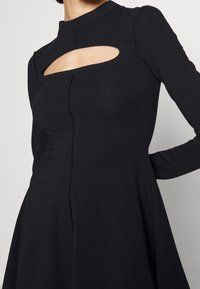 Svart långärmad klänning med utskärning vid bröstet, figurnära bodice och utsvängd kjol; slät tyg med solid textur och sömdetaljer.