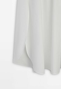 Tessuto bianco e leggero che si drappeggia delicatamente con una texture liscia. Presenta un orlo arrotondato e sottili spacchi laterali per facilitare i movimenti.
