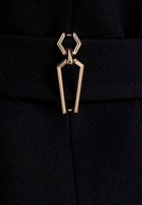 Czarna tkanina o fakturze została ozdobiona złotą broszką w kształcie pająka, co dodaje projektowi charakterystycznego akcentu.