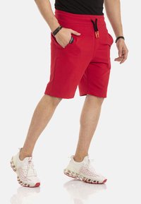 Rode katoenen shorts met elastische taille en trekkoord, voorzien van zijzakken en een enkel-lange snit, gecombineerd met wit-rode sneakers.