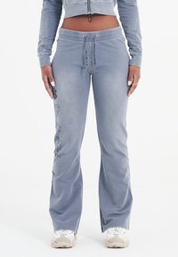 Lichtblauwe joggingbroek met een relaxte pasvorm, een koordsluiting in de taille en bloemgraphic accenten aan de zijkant. Zachte stof met een lichte glans.