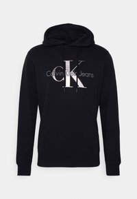 Felpa nera con cappuccio dotata di coulisse, tasca a kangaroo frontale e grande logo metallico con la scritta "CK Calvin Klein Jeans" stampata sul davanti.
