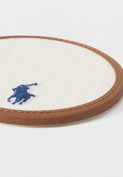 Στρογγυλή λευκή υφασμάτινη θήκη για ποτήρι με μπλε κεντητό λογότυπο αλόγου και αναβάτη, περιτριγυρισμένη από καφέ δερμάτινο περίγραμμα με ραφές.