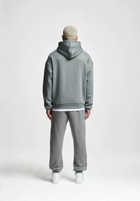 Felpa grigia con cappuccio, dal taglio rilassato, tessuto testurizzato e spalle scese; abbinata a pantaloni da tuta grigi e sneakers bianche.