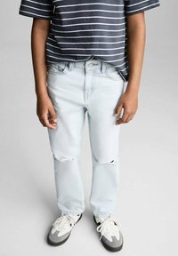 Svetlo modri raztrgani kavbojke z udobnim krojem, v kombinaciji z mornarsko modro majico s kratkimi rokavi z vodoravnimi črtami in sivimi supergami.