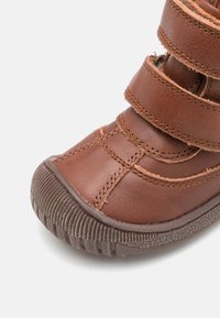 Botte en cuir marron avec une surface texturée, trois fermetures à sangle et une semelle en caoutchouc avec un motif nervuré pour l'adhérence.