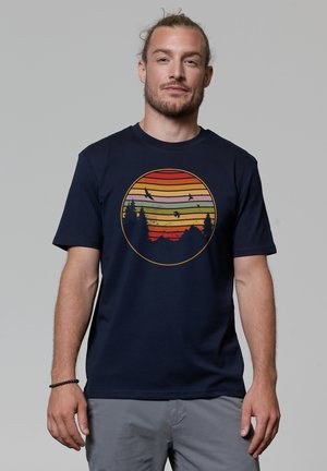 Navyblaues T-Shirt aus Baumwolle mit einem kreisförmigen Grafikdesign, das horizontale Streifen in Rot, Orange und Gelb zeigt und einen Sonnenuntergang mit Bäumen darstellt.