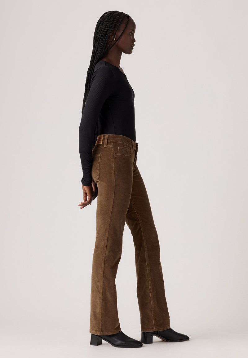 Pantalon en velours côtelé marron avec une coupe évasée, doté de poches avant et d'une finition texturée, associé à un haut noir à manches longues et des bottes à talons.