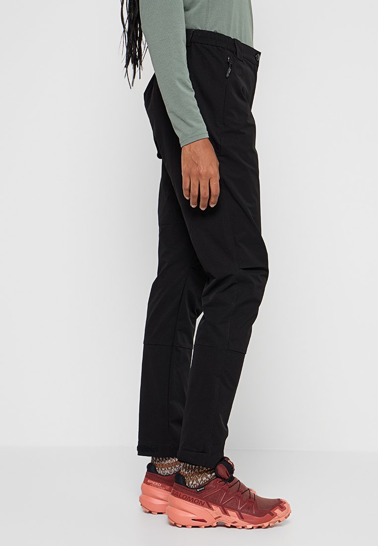 Czarne spodnie outdoorowe o luźnym kroju, z zamkiem błyskawicznym w kieszeni i elastyczną talią, zestawione z czerwonymi butami trekkingowymi i wzorzystymi skarpetkami.