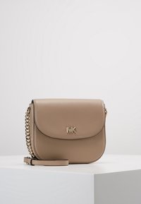 Beige nahkainen olkalaukku kaarevalla muotoilulla, kultasävyisillä yksityiskohdilla, magneettisella läpällä ja ketjuhihnalla.