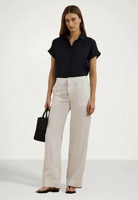 Melna īsām piedurknēm kreklveida blūze apvienota ar krēmkrāsas plaša kāju biksēm, kurām ir aukla jostasvietā un priekšējā kabata. Modelis tur melnu austu somu.