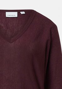 Sweter z dekoltem w kształcie V, długim rękawem w głębokim burgundzie, wykonany z lekkiej, teksturowanej tkaniny. Metka z nazwą marki "COMMA" oraz rozmiarem "S."
