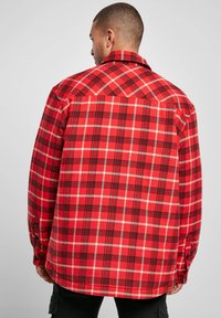 Red and black checkered flannel shirt with visible stitching and buttoned cuffs, featuring a collar and a slightly curved hem.