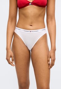 Hvid bomulds-tanga med rød og blå mærket taljebånd. Har en glat tekstur og et design med minimal dækning.