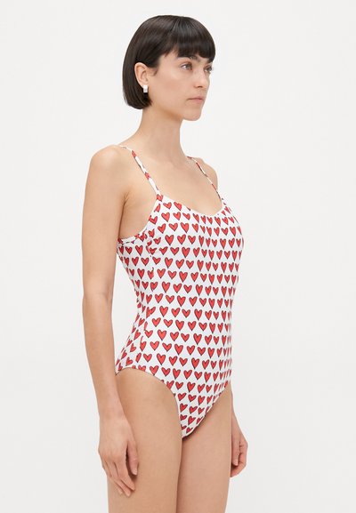 One-piece swimsuit in white with repeated red heart pattern. Features adjustable straps and a fitted design for streamlined appearance.