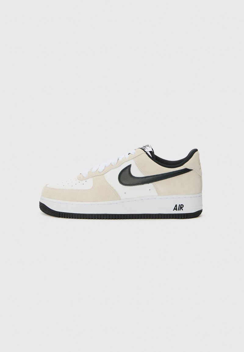Sneakers with a light beige suede and white leather upper, black Nike swoosh, black accents, and a white rubber sole featuring "AIR" branding.